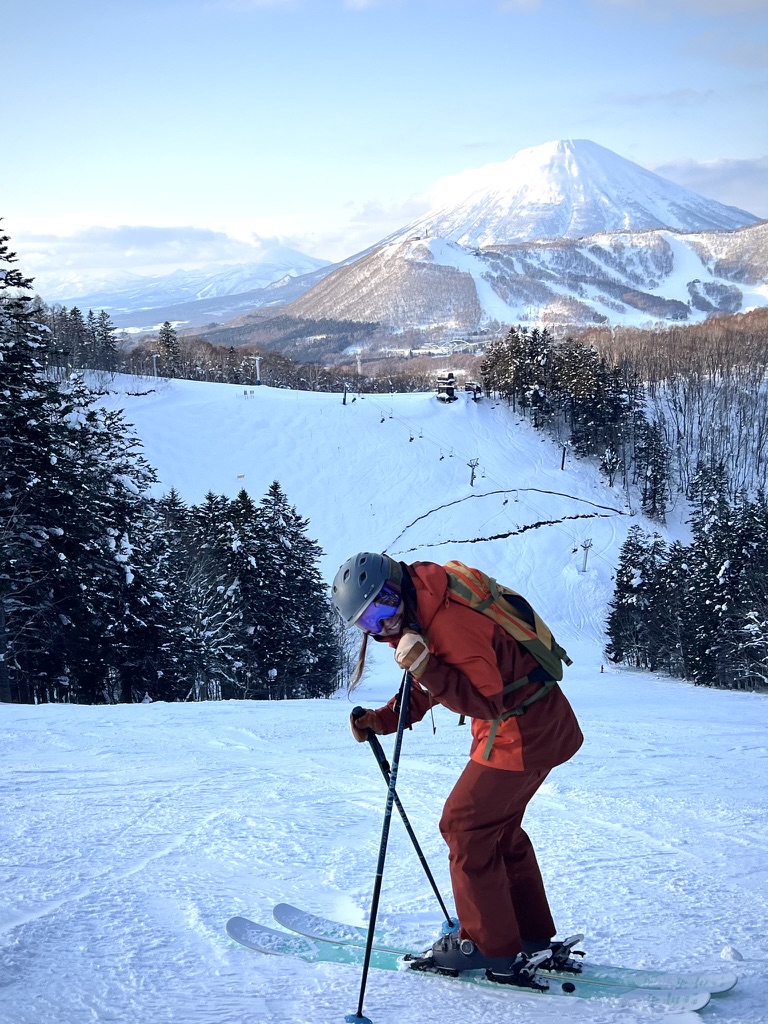Kaylea skiing down a snowy run with a mountain peak behind her